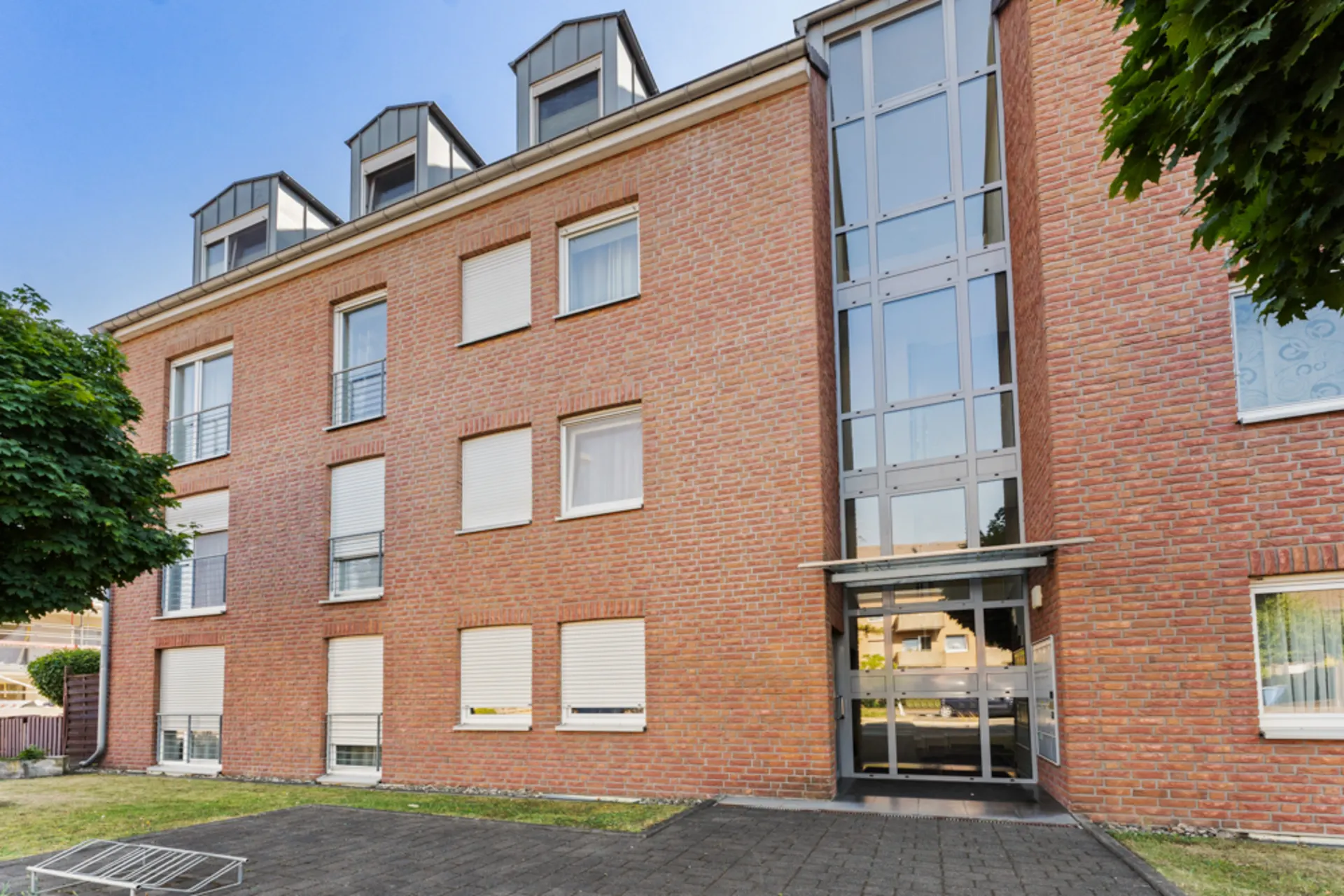 Mehrfamilienhaus mit roter Klinkerfassade und großem verglastem Eingangsbereich.