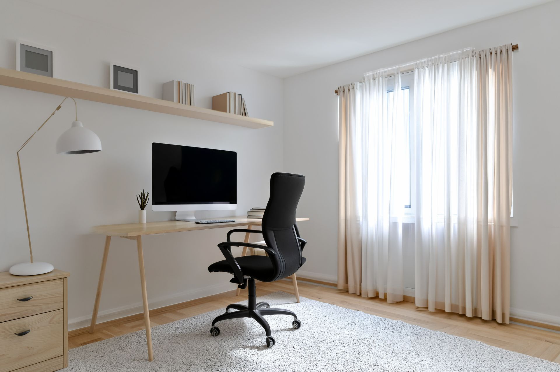 Helles Arbeitszimmer mit Schreibtisch, Bürostuhl, Computer und großem Fenster mit Vorhängen.