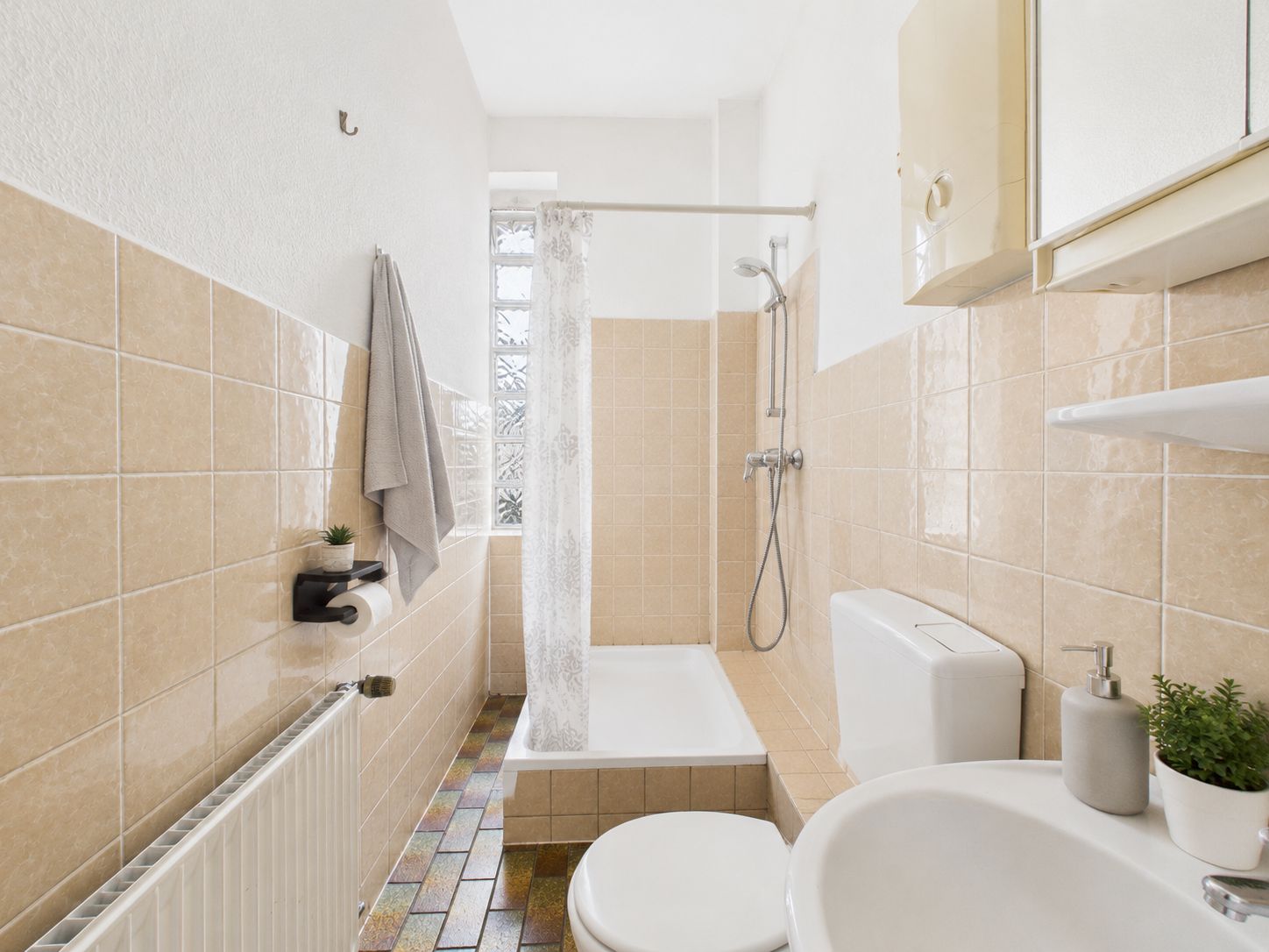 Helles Badezimmer mit Dusche, Toilette, Waschbecken und beigen Fliesen.