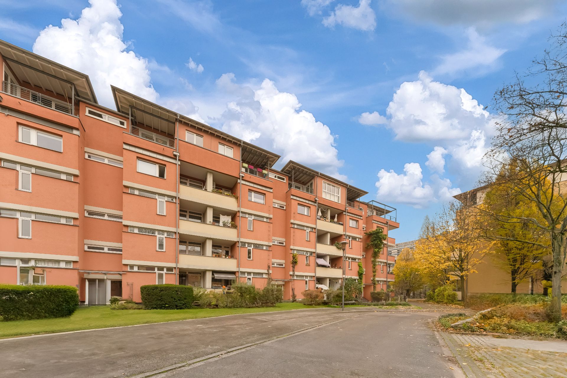 Mehrstöckiges Wohngebäude mit orangefarbener Fassade und Balkonen, davor Straße und Bäume.