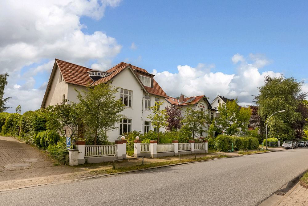 Großes weißes Wohnhaus mit rotem Dach, Vorgarten und Einfahrt an ruhiger Straße.