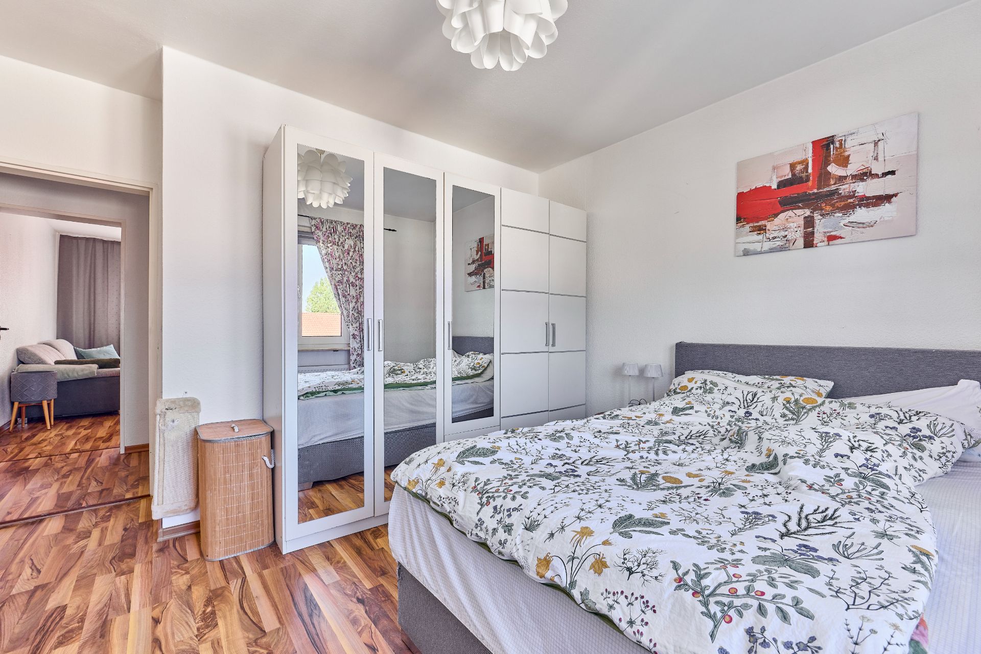 Helles Schlafzimmer mit Doppelbett, Kleiderschrank mit Spiegeln und Holzboden.