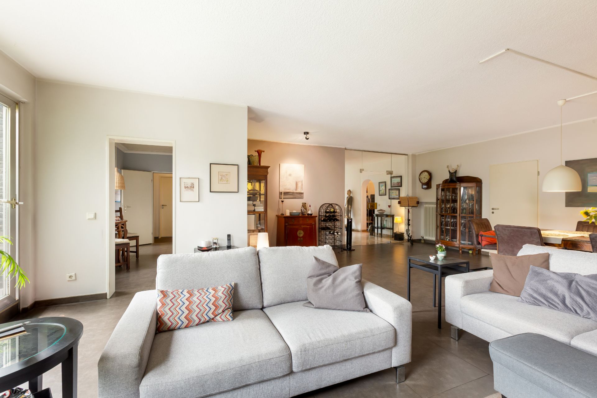 Helles Wohnzimmer mit grauen Sofas, Couchtisch und Essbereich im Hintergrund.