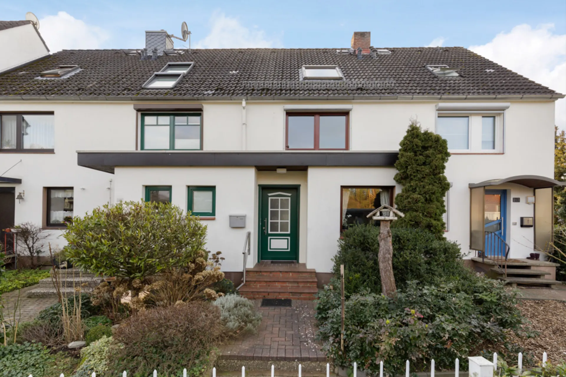 Reihenhaus mit grünem Eingang, Vorgarten und Buschwerk vor dem Haus.
