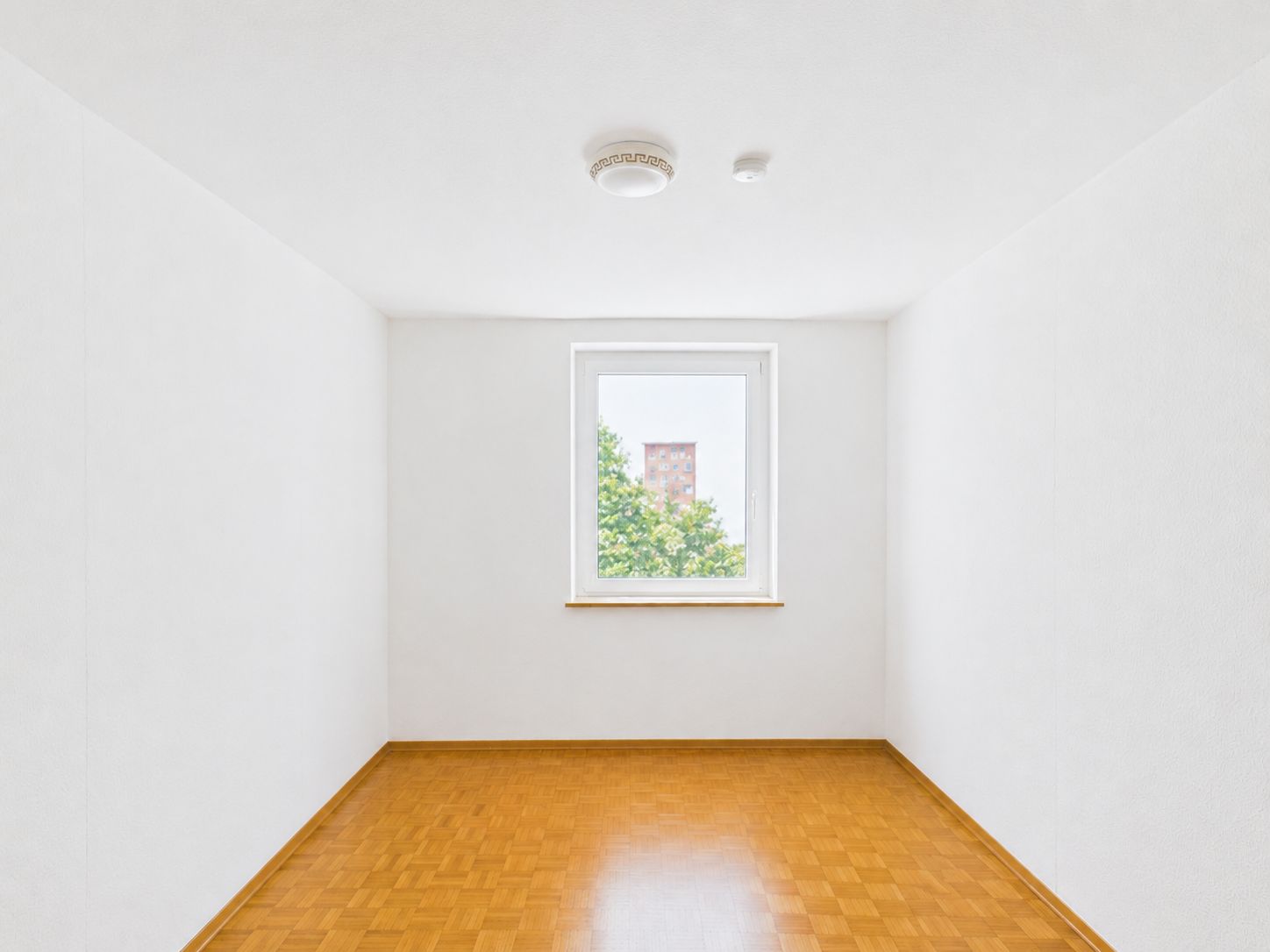 Leeres Zimmer mit weiß gestrichenen Wänden, Holzfußboden und Fenster.