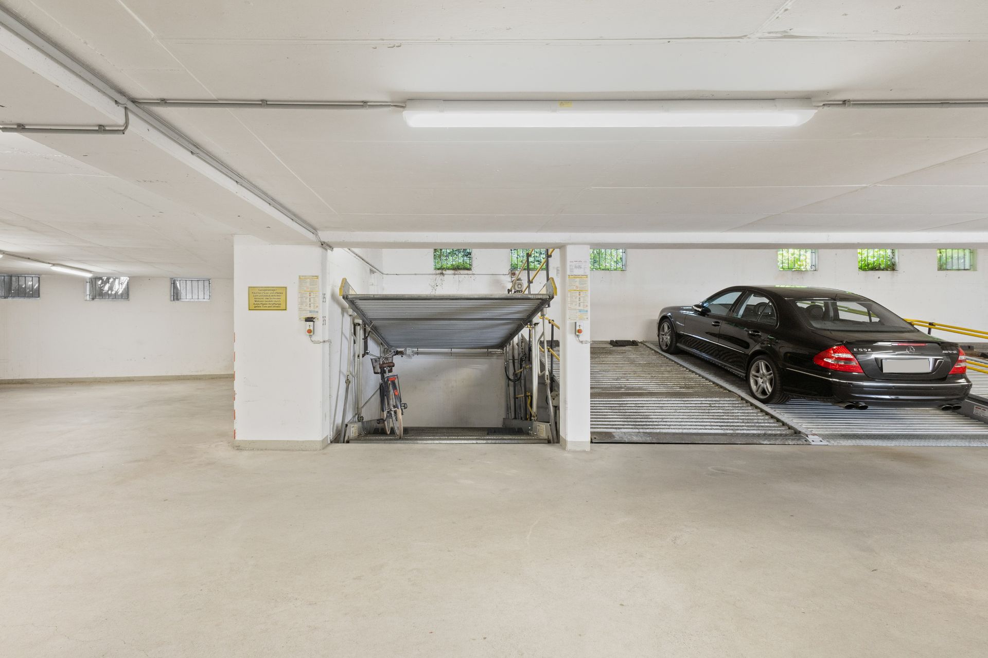 Tiefgarage mit leerem Boden, einem Fahrrad und einem schwarzen Auto auf einem Parksystem.