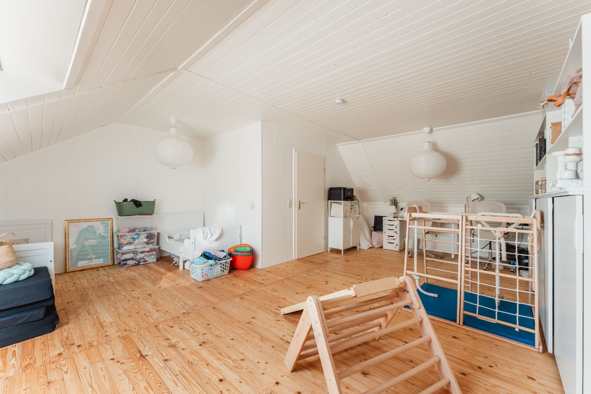 Geräumiges Dachzimmer mit Holzfußboden, Spielgeräten und Schreibtisch unter schräger Decke.