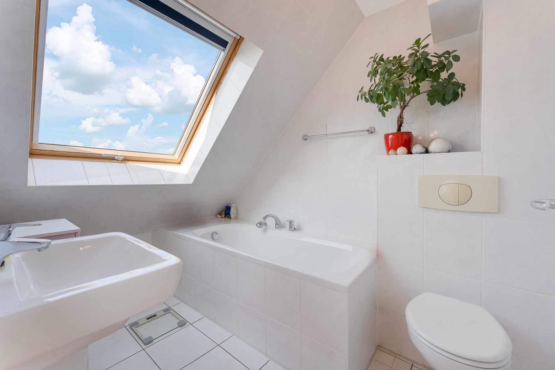 Modernes Badezimmer mit Dachfenster, Badewanne, Waschbecken, Toilette und Pflanze.