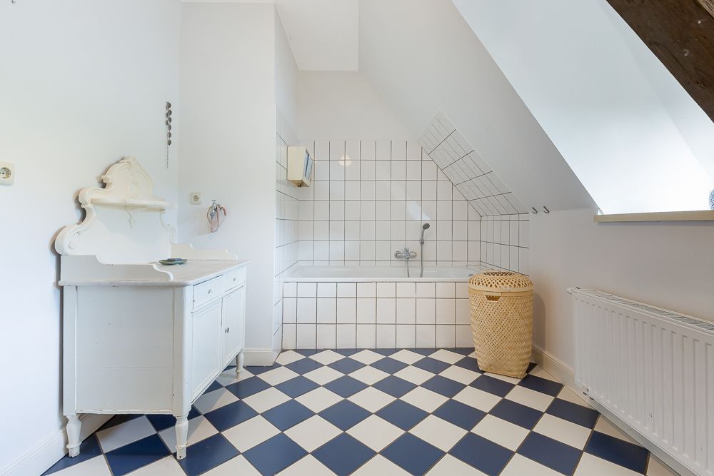 Helles Badezimmer mit Badewanne, weißem Waschtisch und blau-weiß kariertem Fliesenboden.