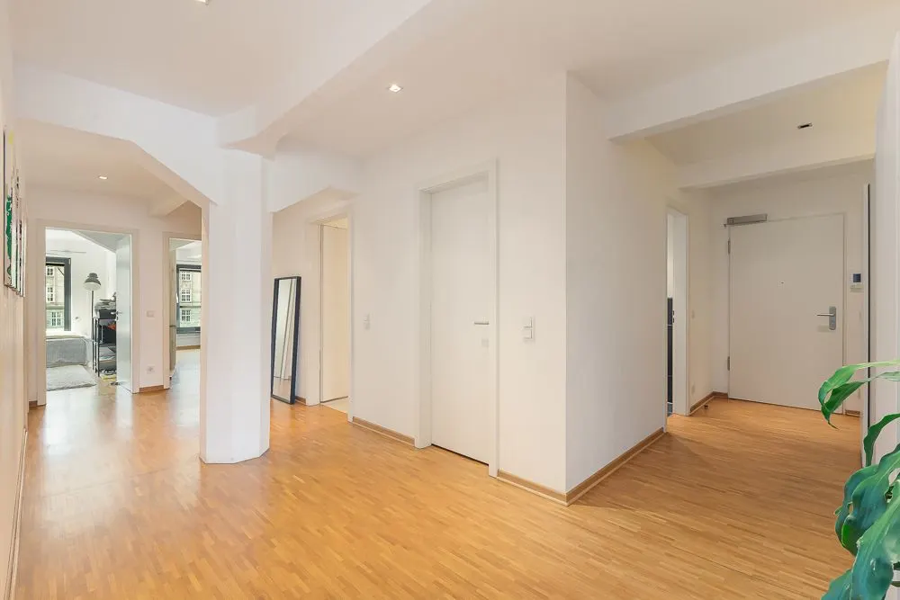 Heller Flur mit Holzboden, weißen Wänden und mehreren Türen, Spiegel an der Wand.