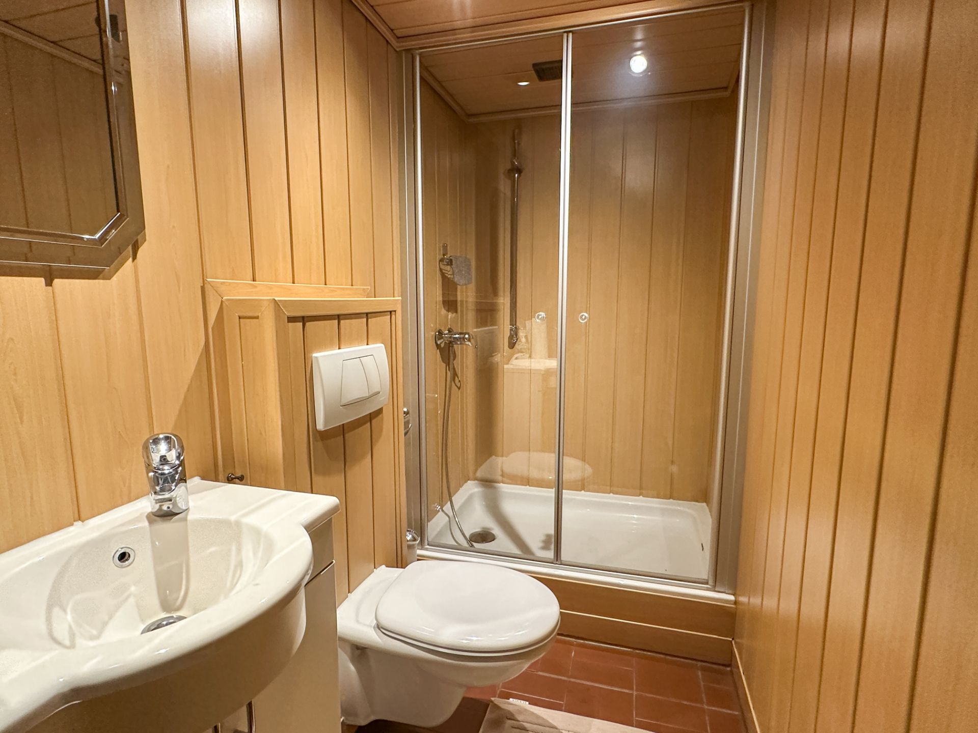 Badezimmer mit Holzverkleidung, Dusche mit Glastür, Waschbecken und Toilette.