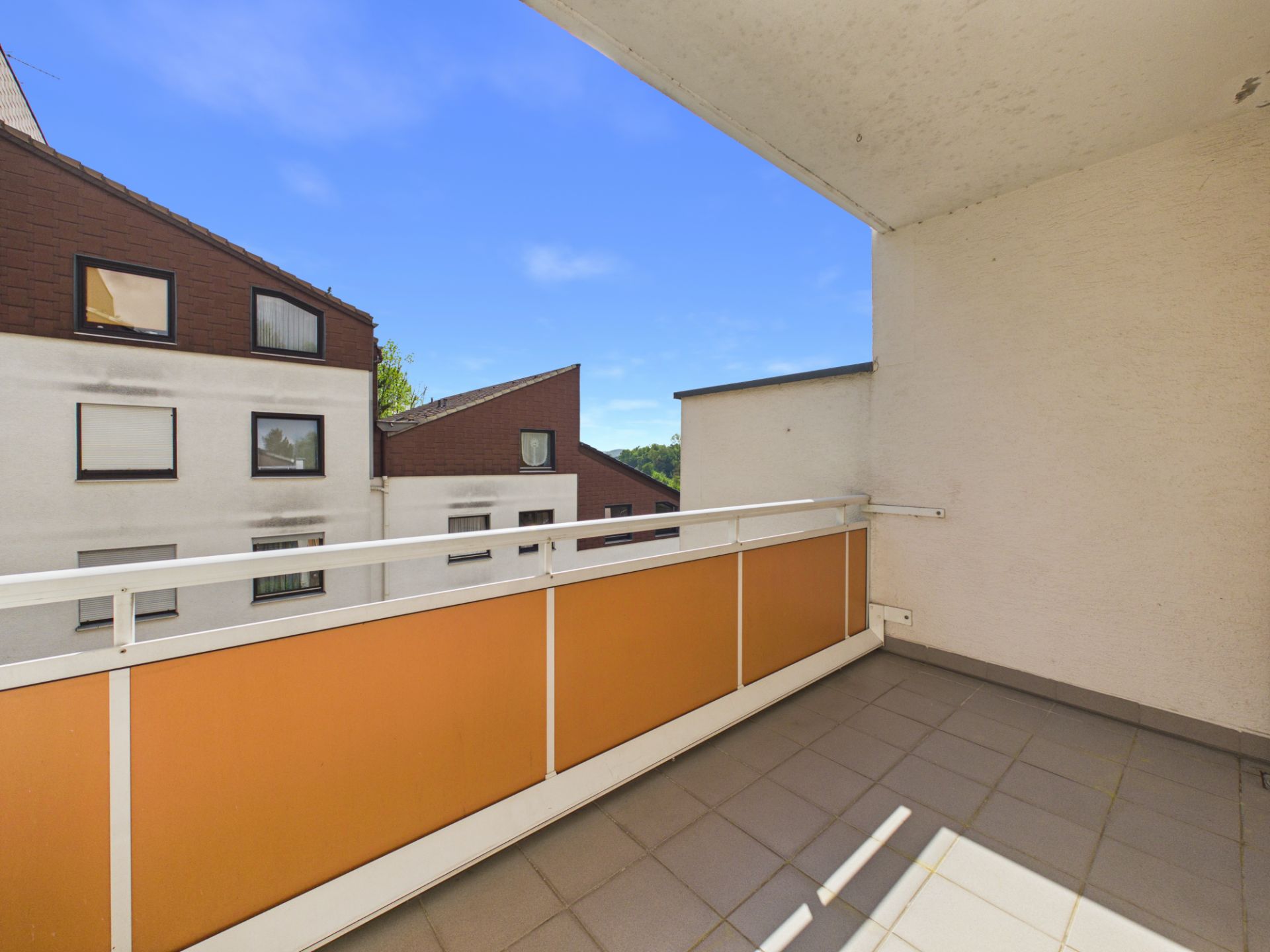 Überdachter Balkon mit oranger Brüstung und Blick auf Nachbargebäude.