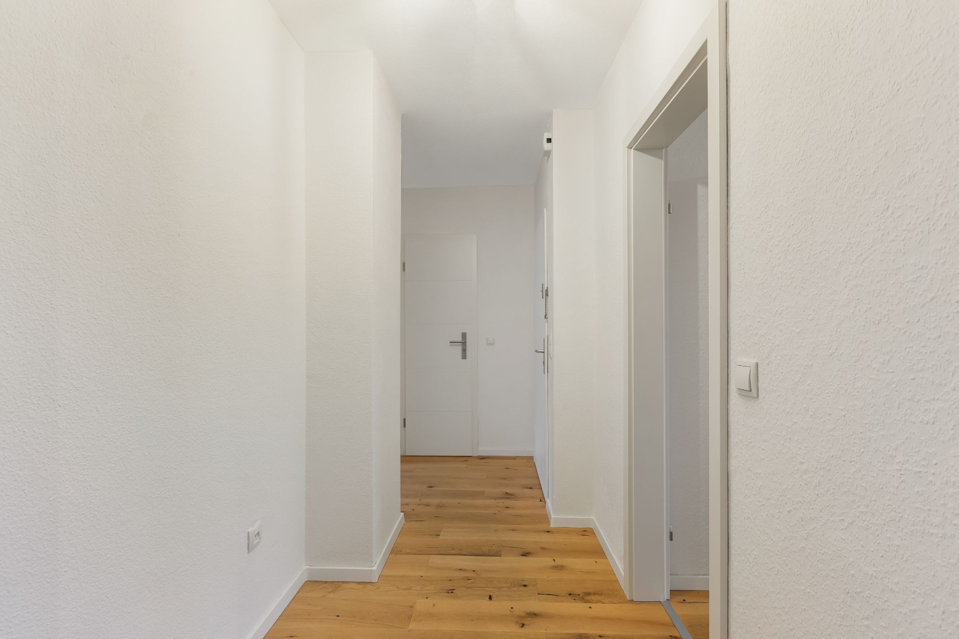 Heller Flur mit Holzboden und weißen Wänden, Türen an der rechten Seite.