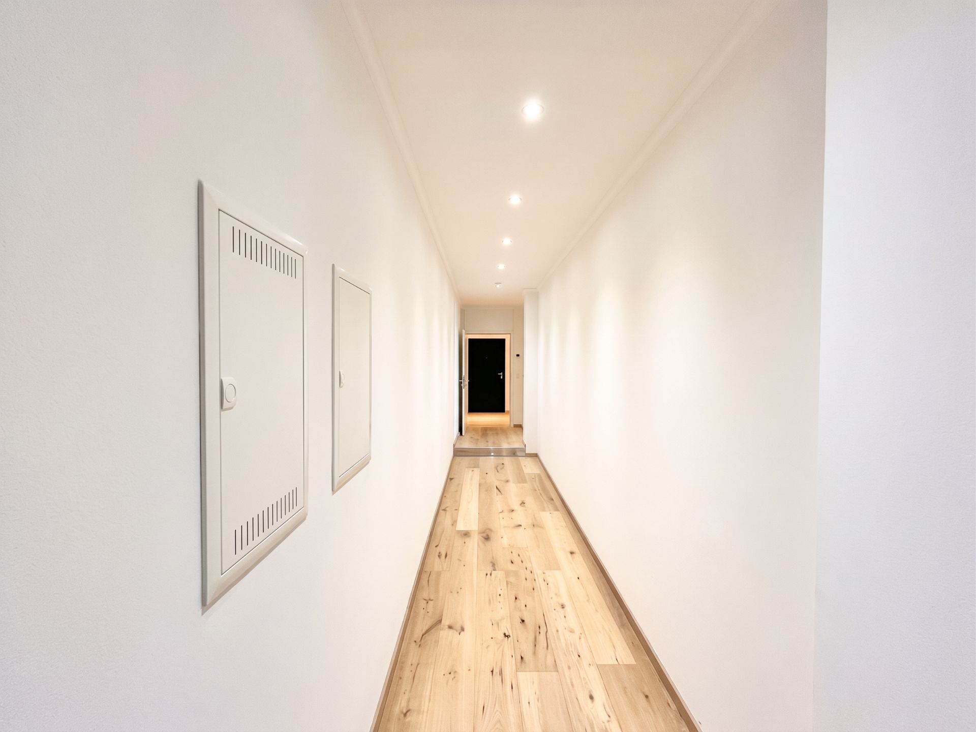 Langer, heller Flur mit Holzboden und weißen Wänden in einem Wohngebäude.