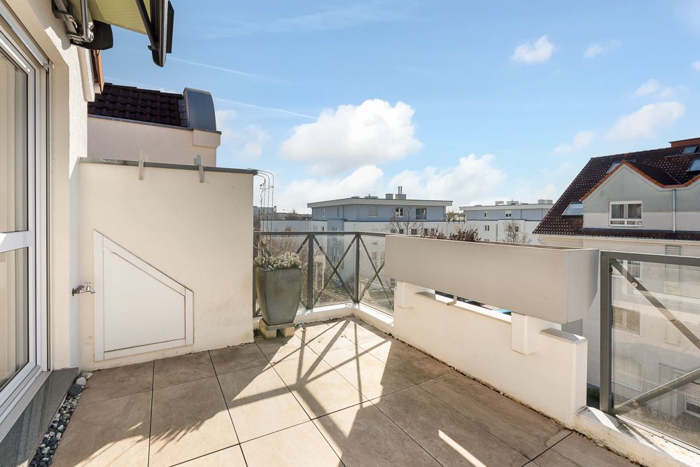 Helle Dachterrasse mit Fliesenboden, Glasgeländer und Blick auf benachbarte Wohngebäude.
