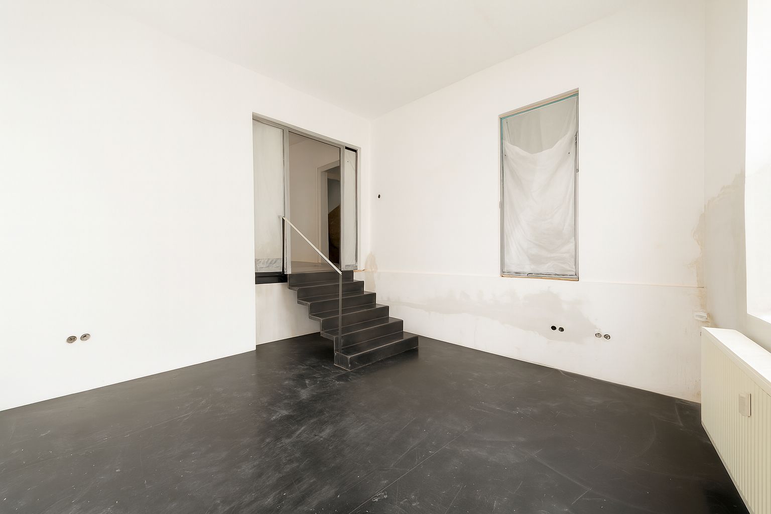 Leerer Raum mit schwarzem Boden und einer kleinen Treppe zu einer höheren Ebene.