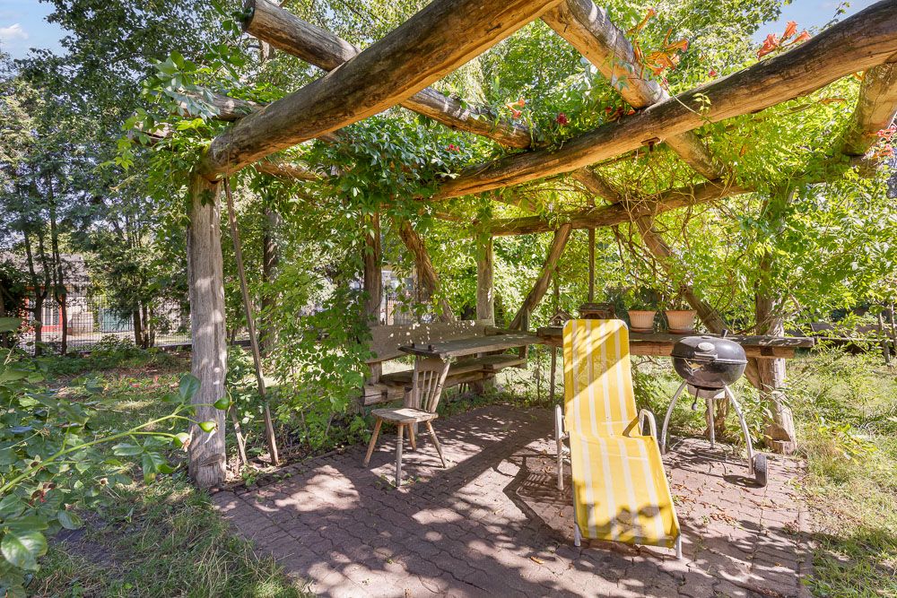 Überdachte Holzterrasse mit Bank, Stühlen, Grill und gelber Liege im Garten.