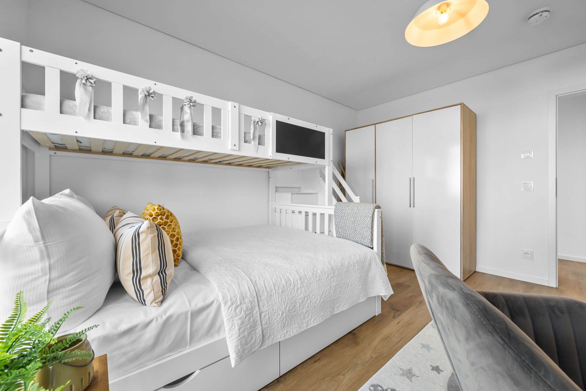 Modernes Schlafzimmer mit Hochbett, Doppelbett, grauem Stuhl, Pflanze und weißem Kleiderschrank.