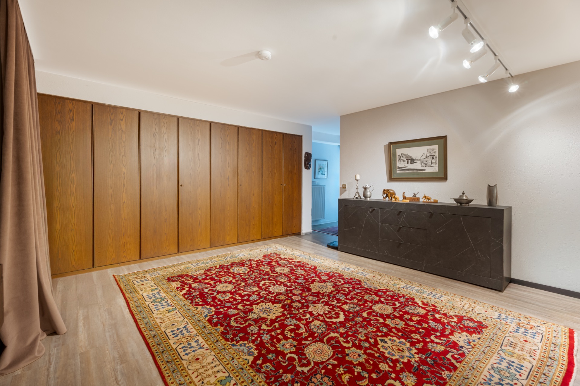 Raum mit großem bunten Teppich, Holzwandschrank und Kommode mit Dekorationen an der Wand.
