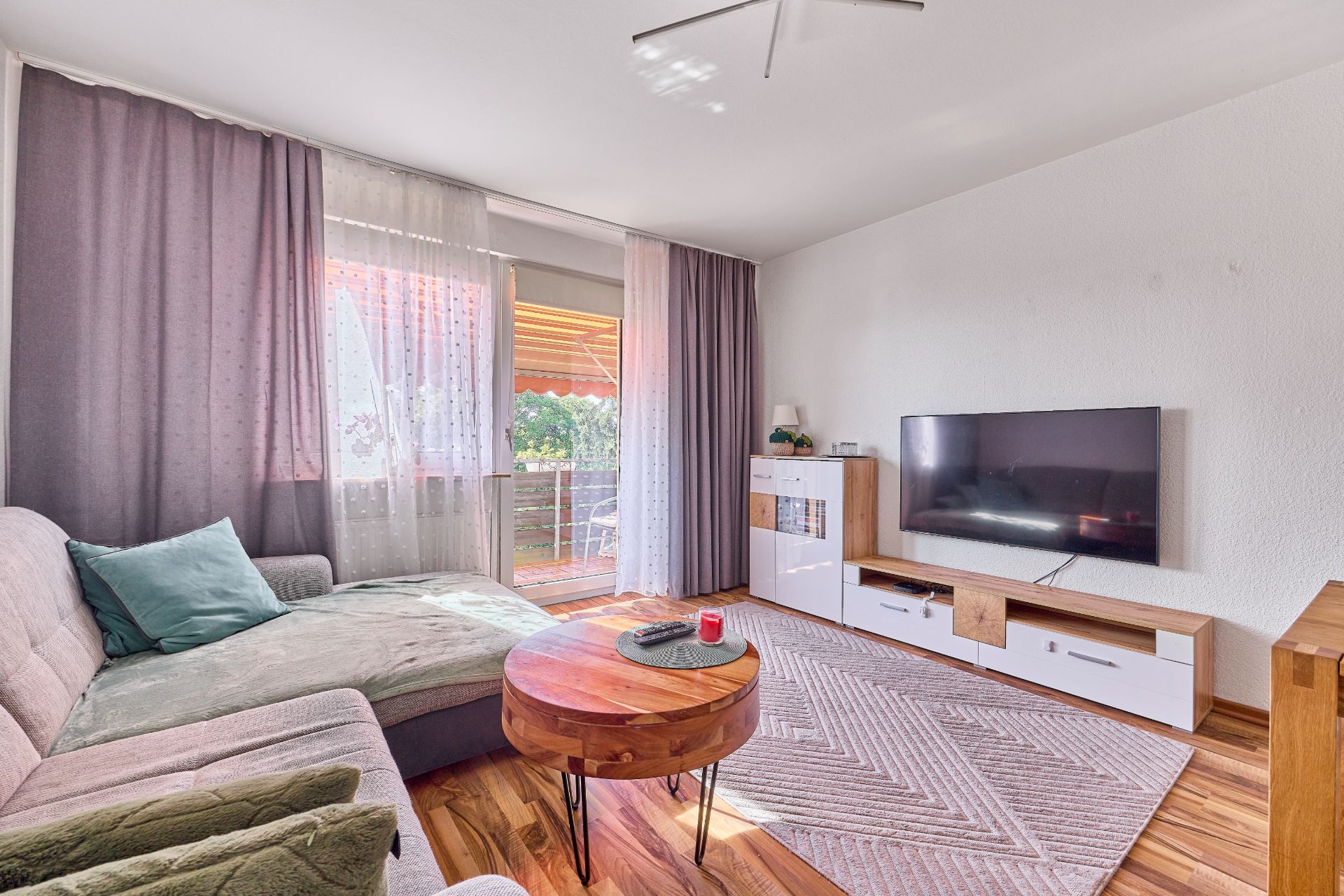 Modernes Wohnzimmer mit Ecksofa, Couchtisch, Fernseher und Zugang zu einem Balkon.