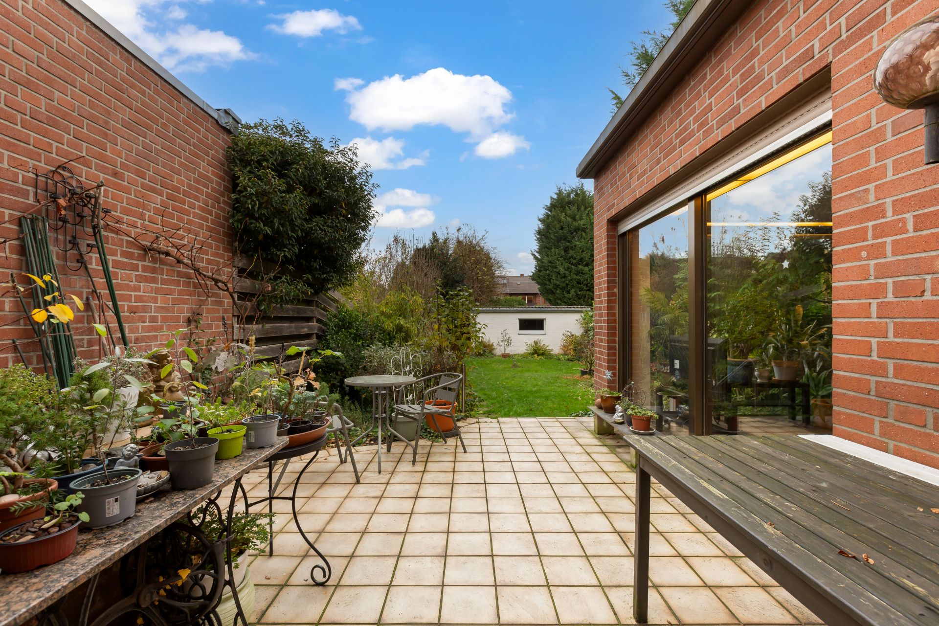 Gepflasterte Terrasse mit Pflanzen, Tisch und Stühlen, angrenzend an Garten und Backsteinwände.