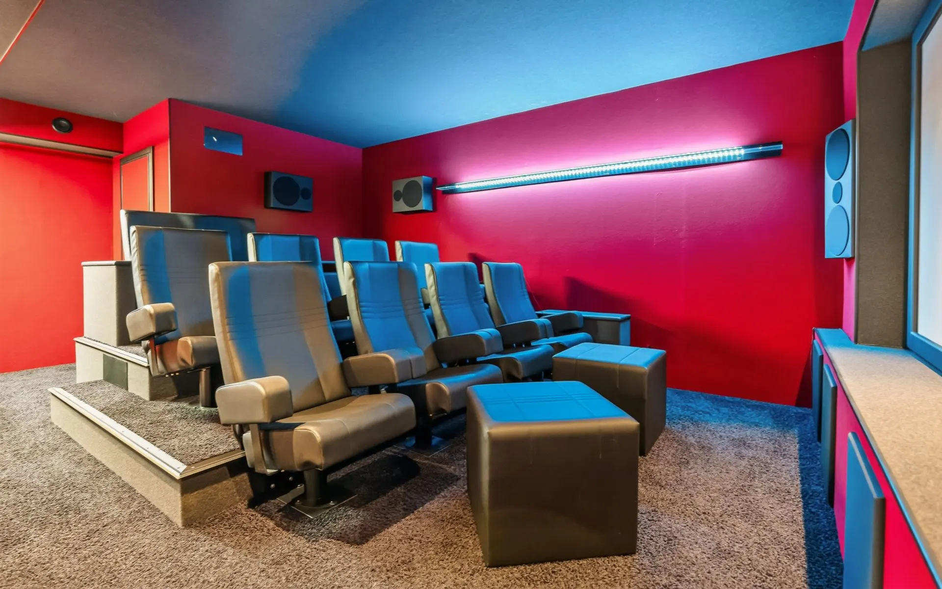 Heimkino mit zwei Reihen Ledersesseln, roter Wand und Lautsprechern an den Wänden.