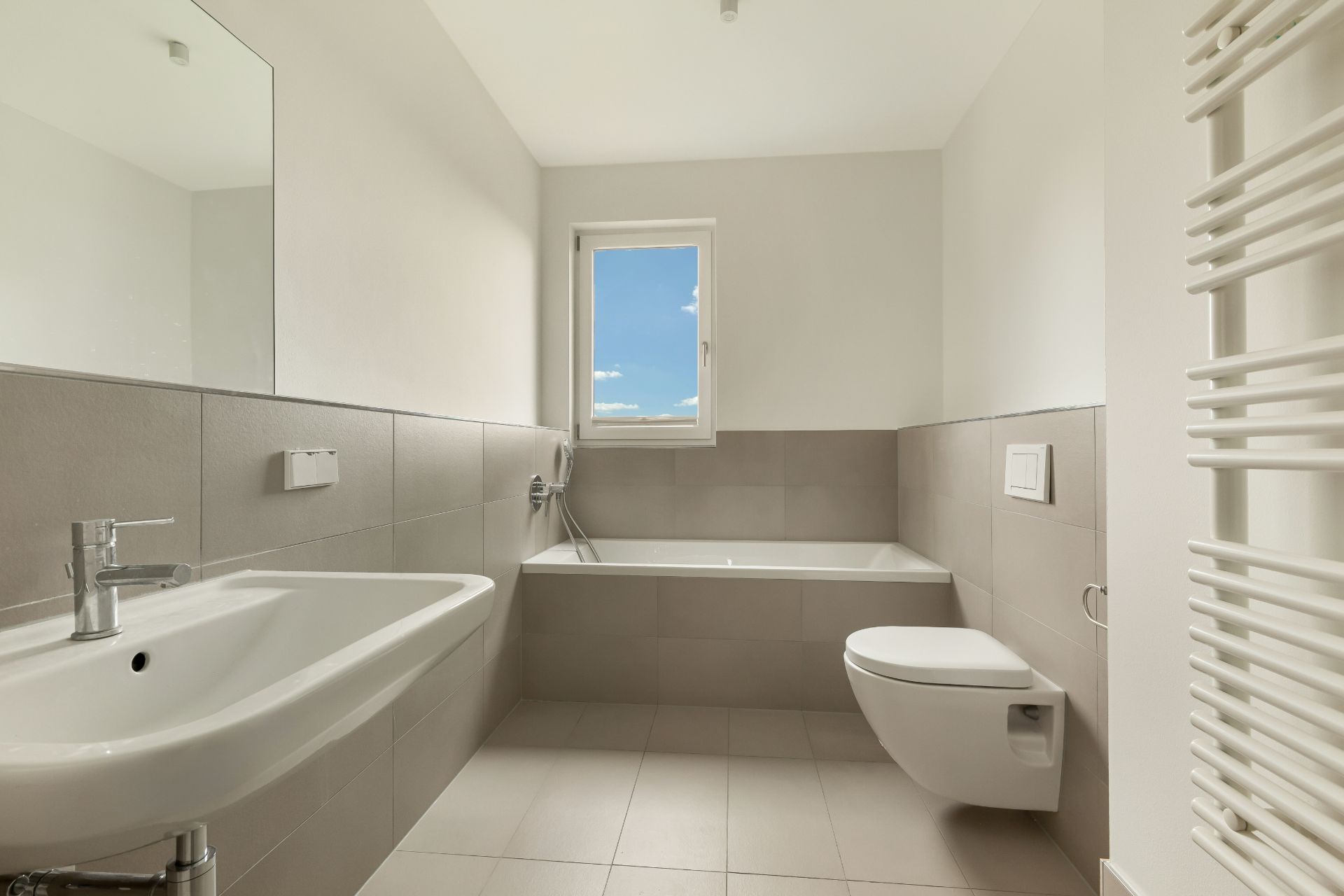 Modernes, helles Badezimmer mit Waschbecken, Badewanne, Toilette und Fenster.