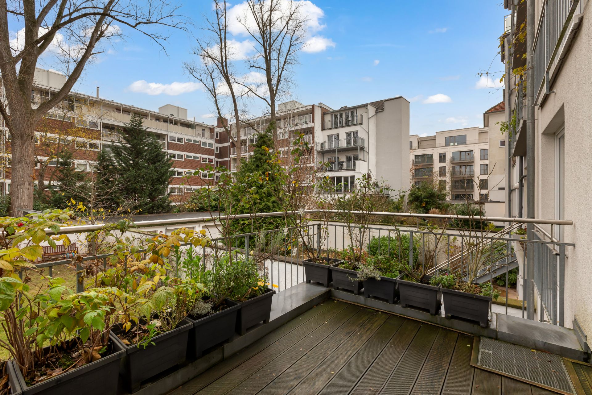 Blick von einem Balkon mit Pflanzenkästen auf eine Wohnanlage mit mehreren Gebäuden.