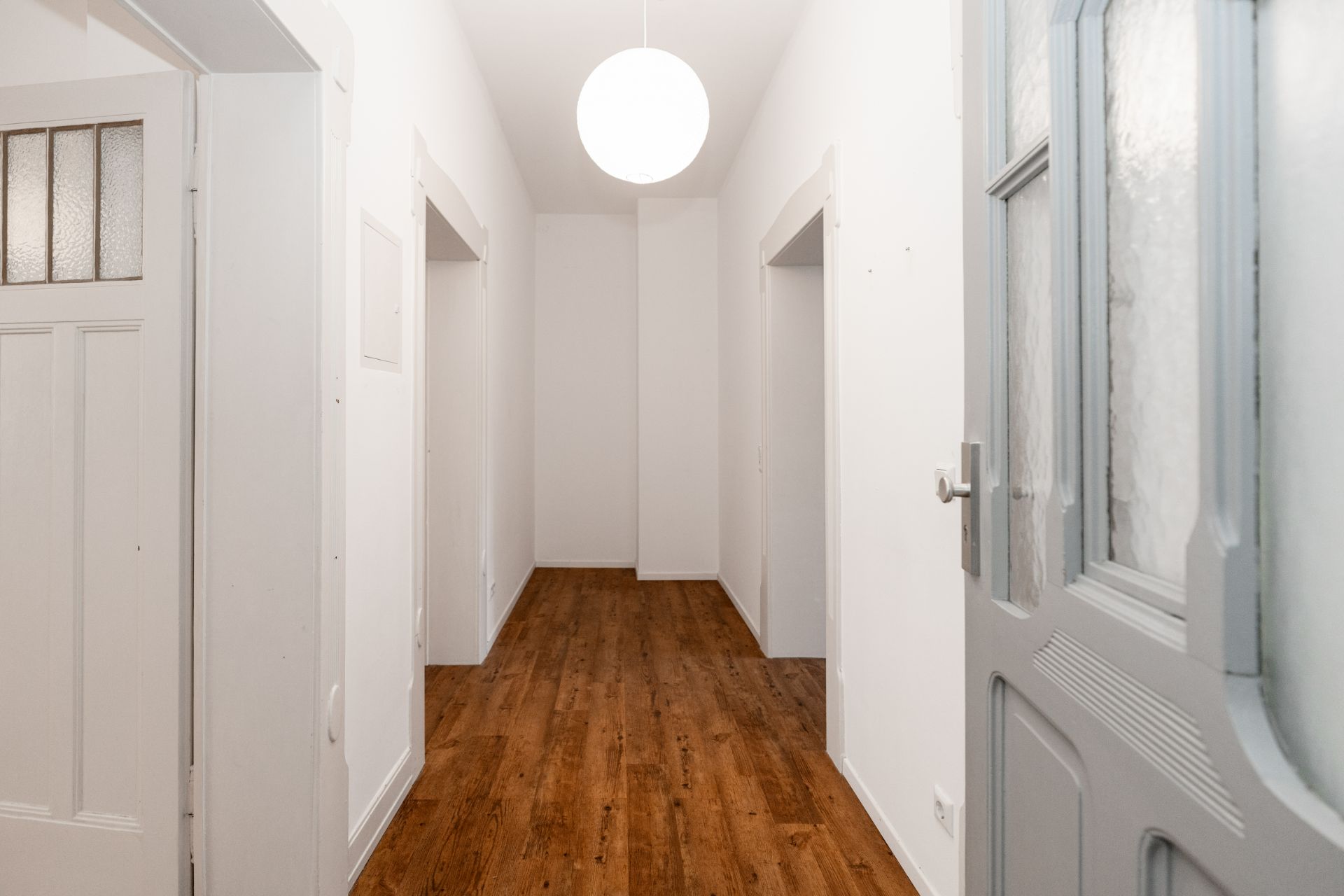 Heller Flur mit Holzboden, weißen Wänden und mehreren offenen Türen.