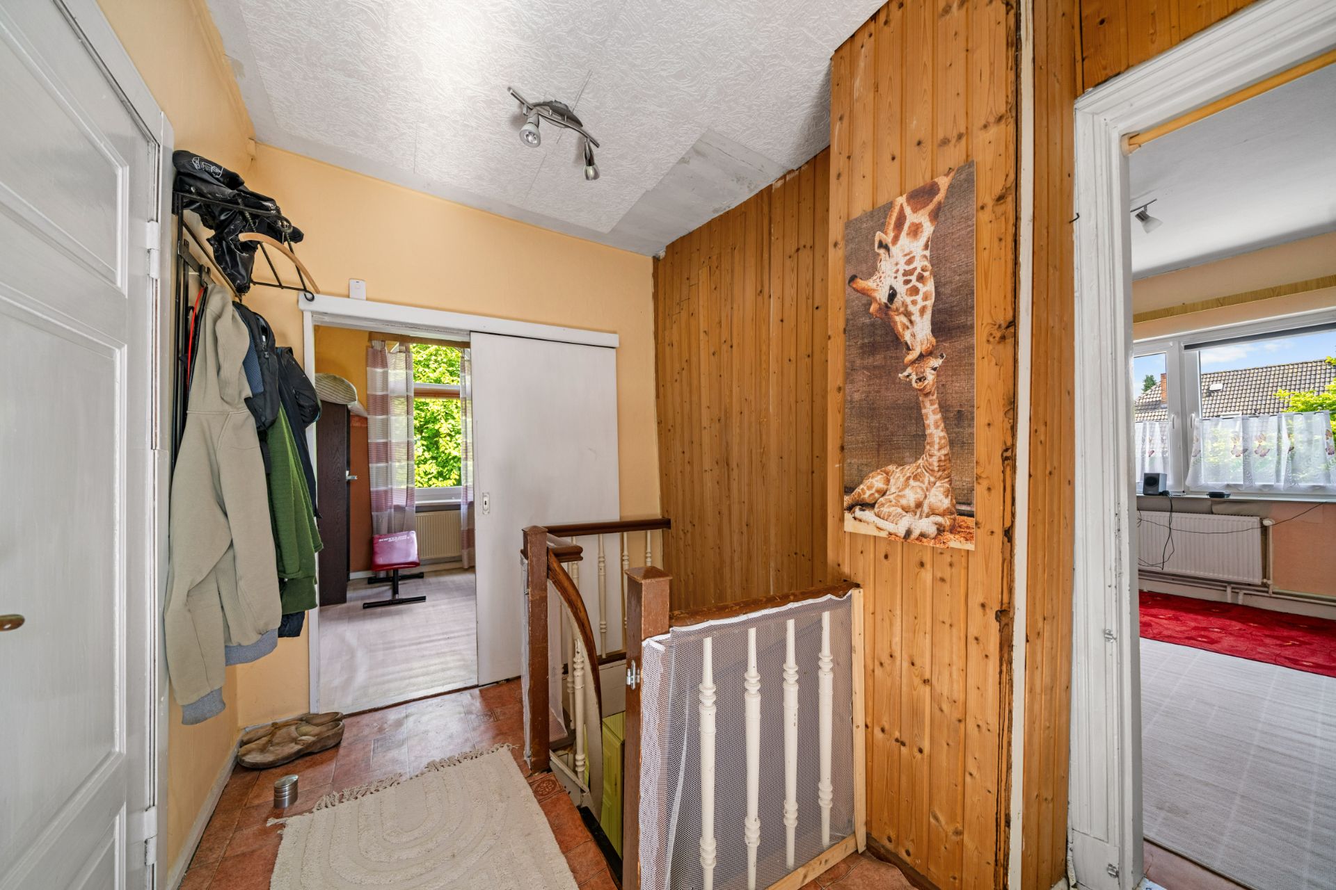Flur mit Holztreppe, Kleiderhaken, Teppich und Bild von zwei Giraffen an der Wand.
