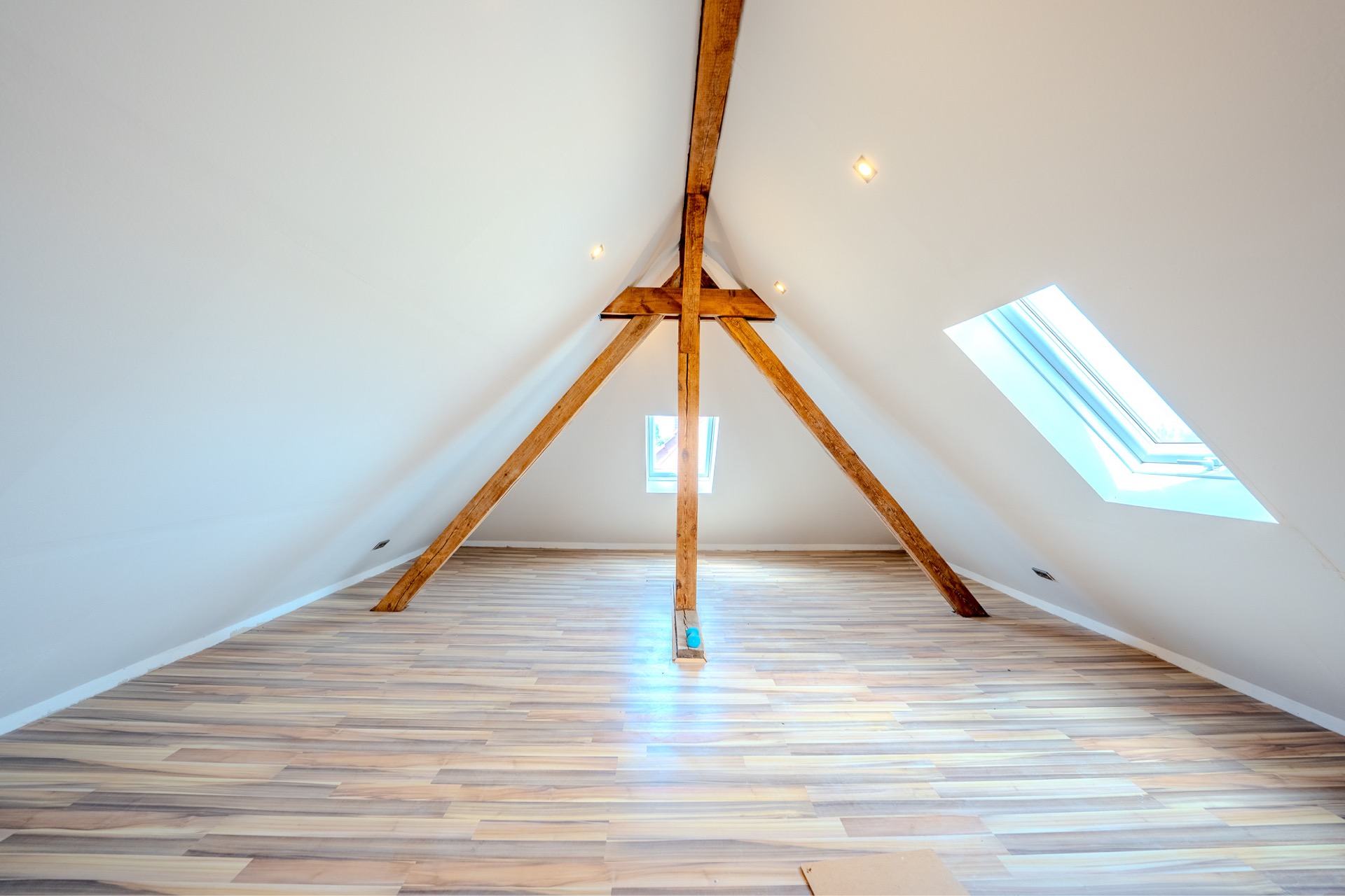 Heller Dachbodenraum mit sichtbaren Holzbalken, Dachfenster und Holzfußboden.