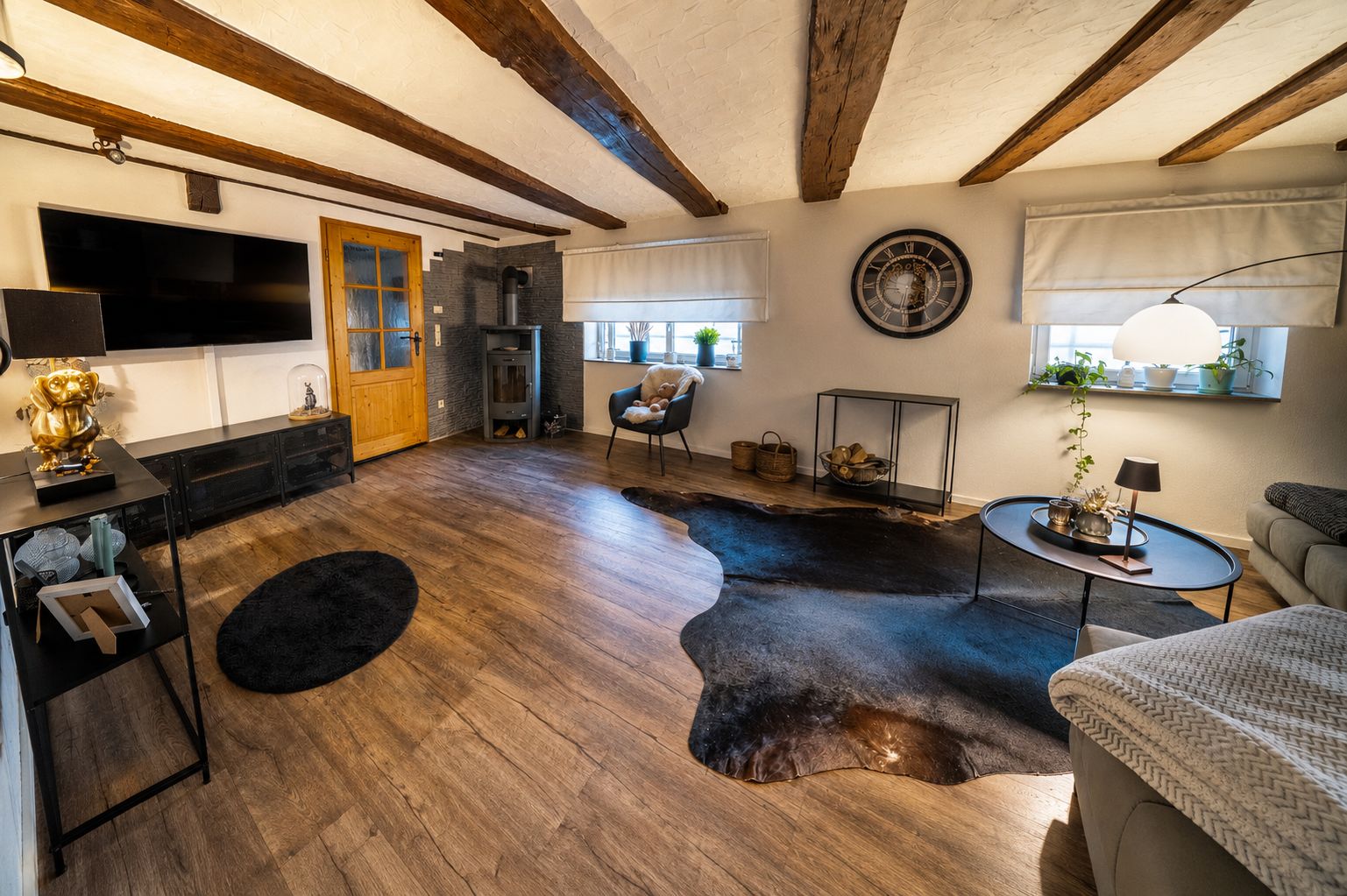 Wohnzimmer mit Holzboden, Holzbalken an der Decke, Sofa, Teppichen und Kaminofen.