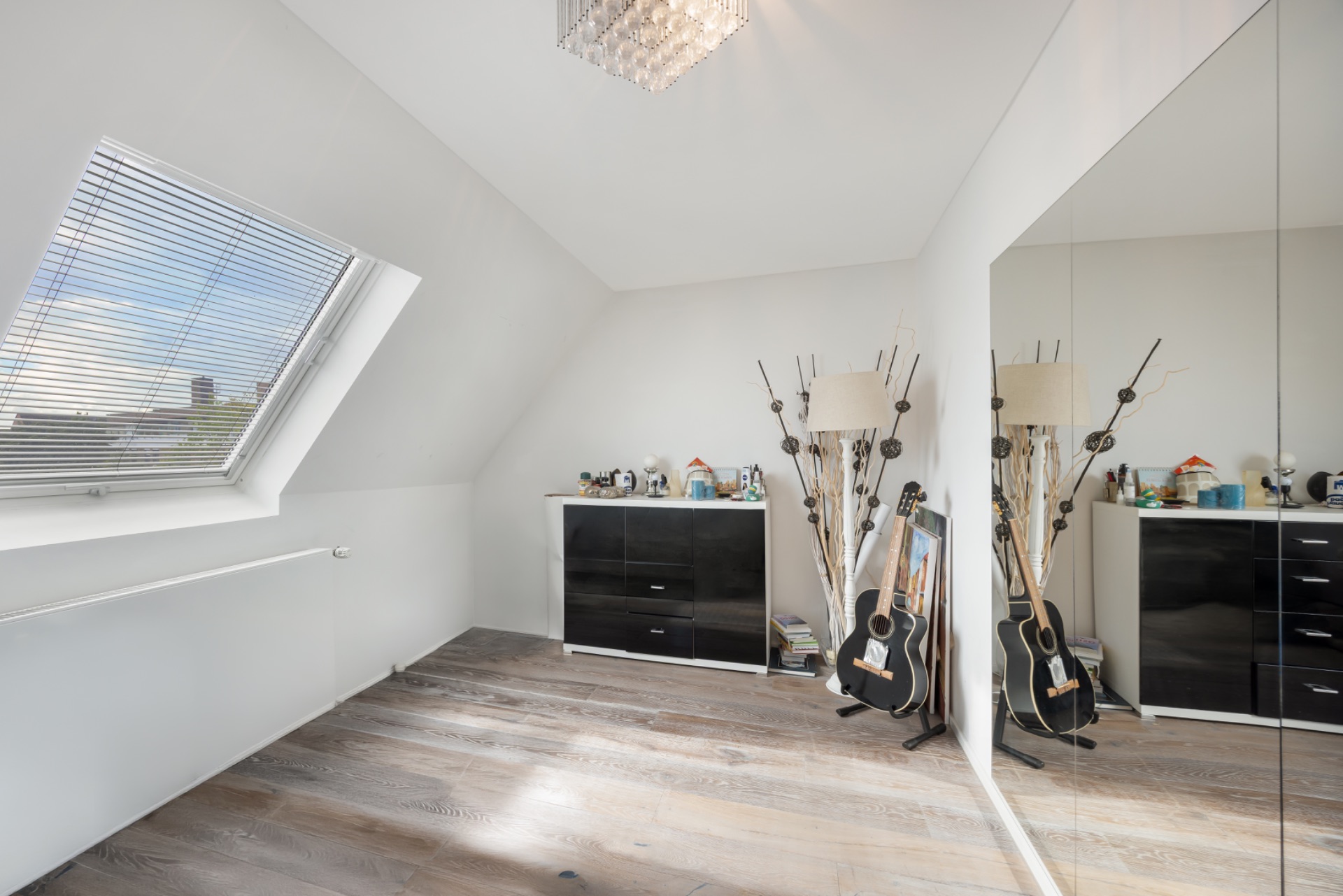 Helles Zimmer mit Dachfenster, Holzboden, Kommode, Spiegelwand und Gitarren.