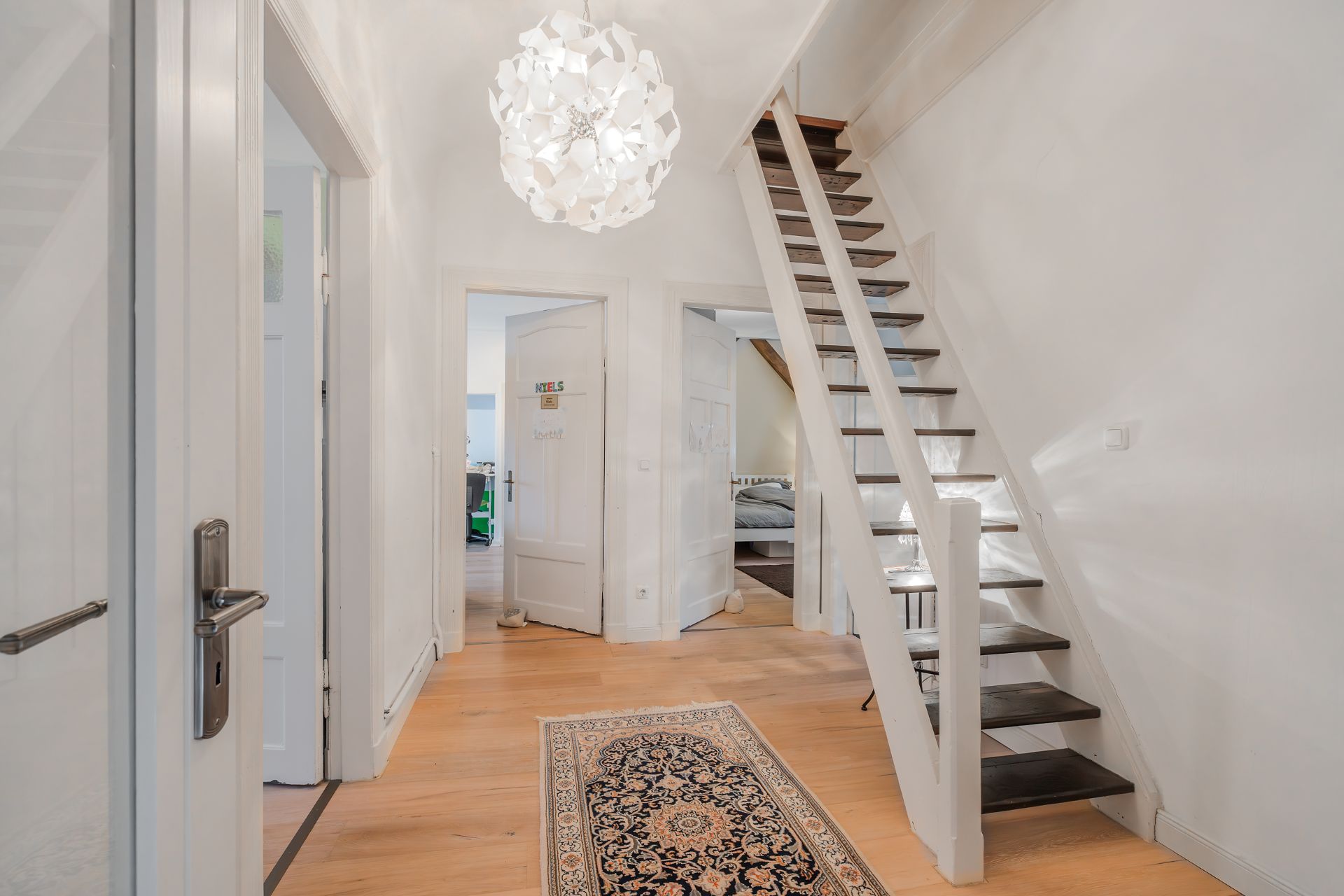 Heller Flur mit Treppe, Teppichläufer und zwei offenen Türen zu angrenzenden Zimmern.