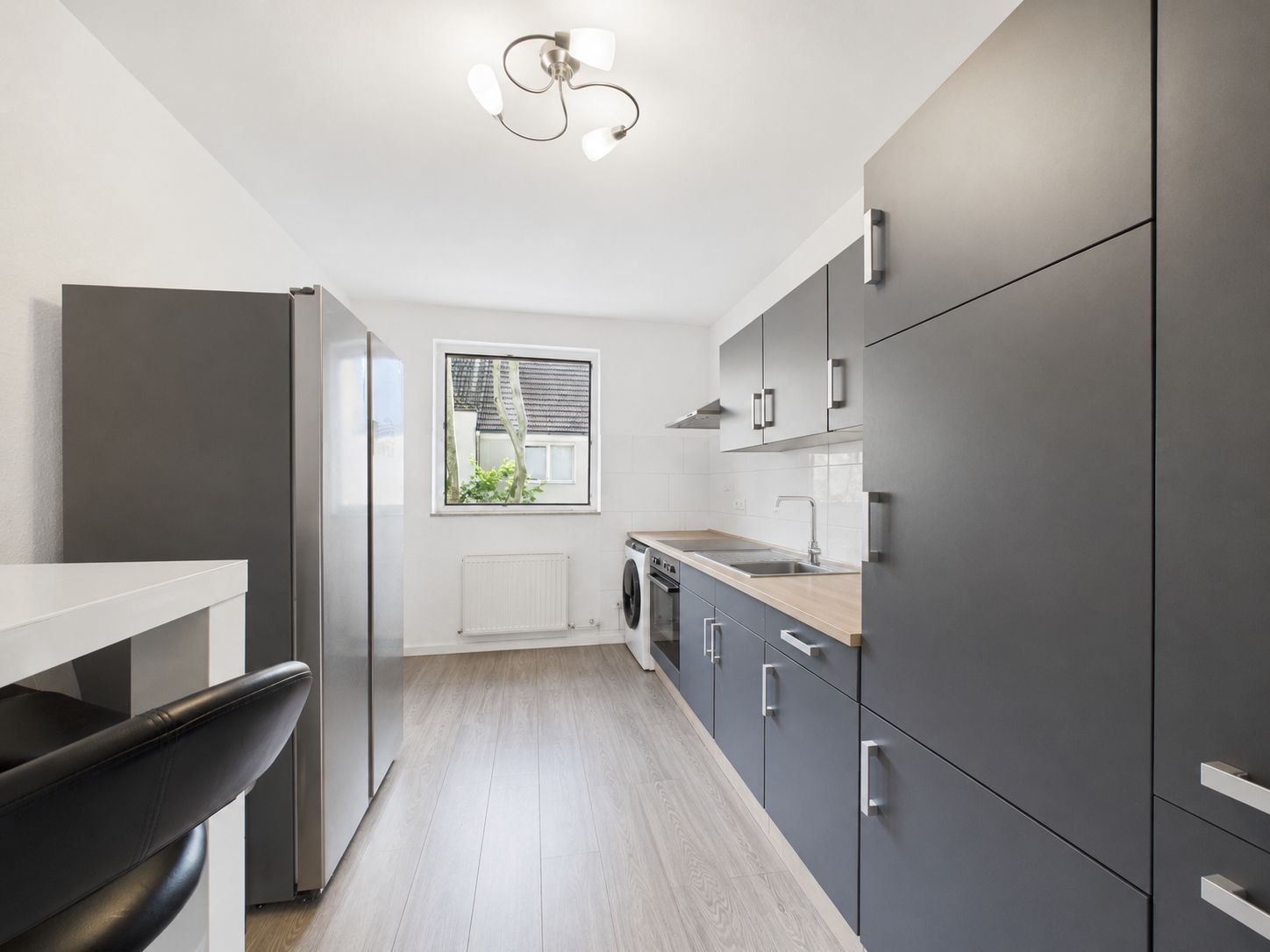 Moderne Küche mit grauen Einbauschränken, Holzarbeitsfläche, großem Fenster und hellem Boden.
