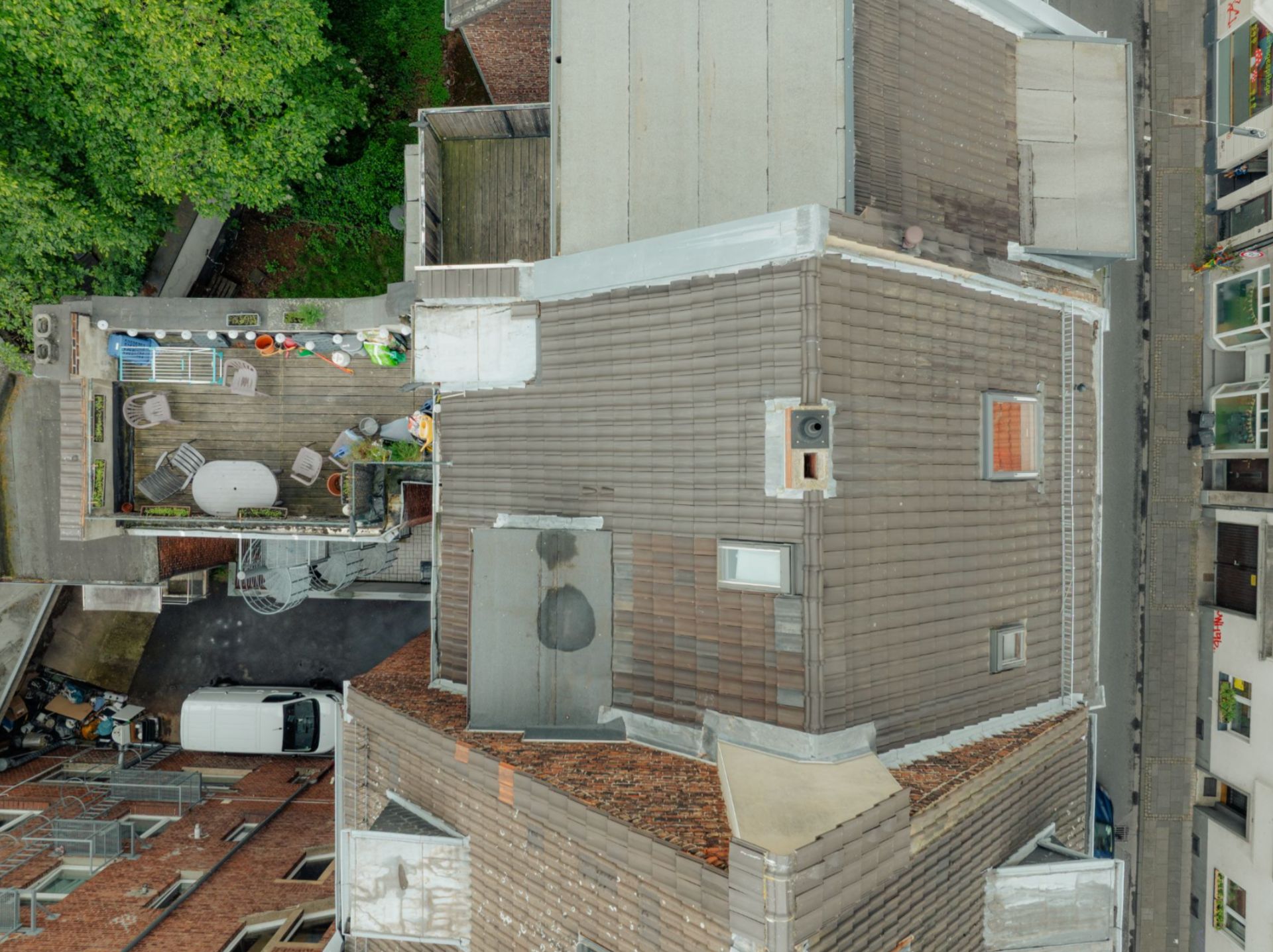Draufsicht auf ein Wohnhaus mit Dachterrasse, Möbeln und einigen Pflanzen.