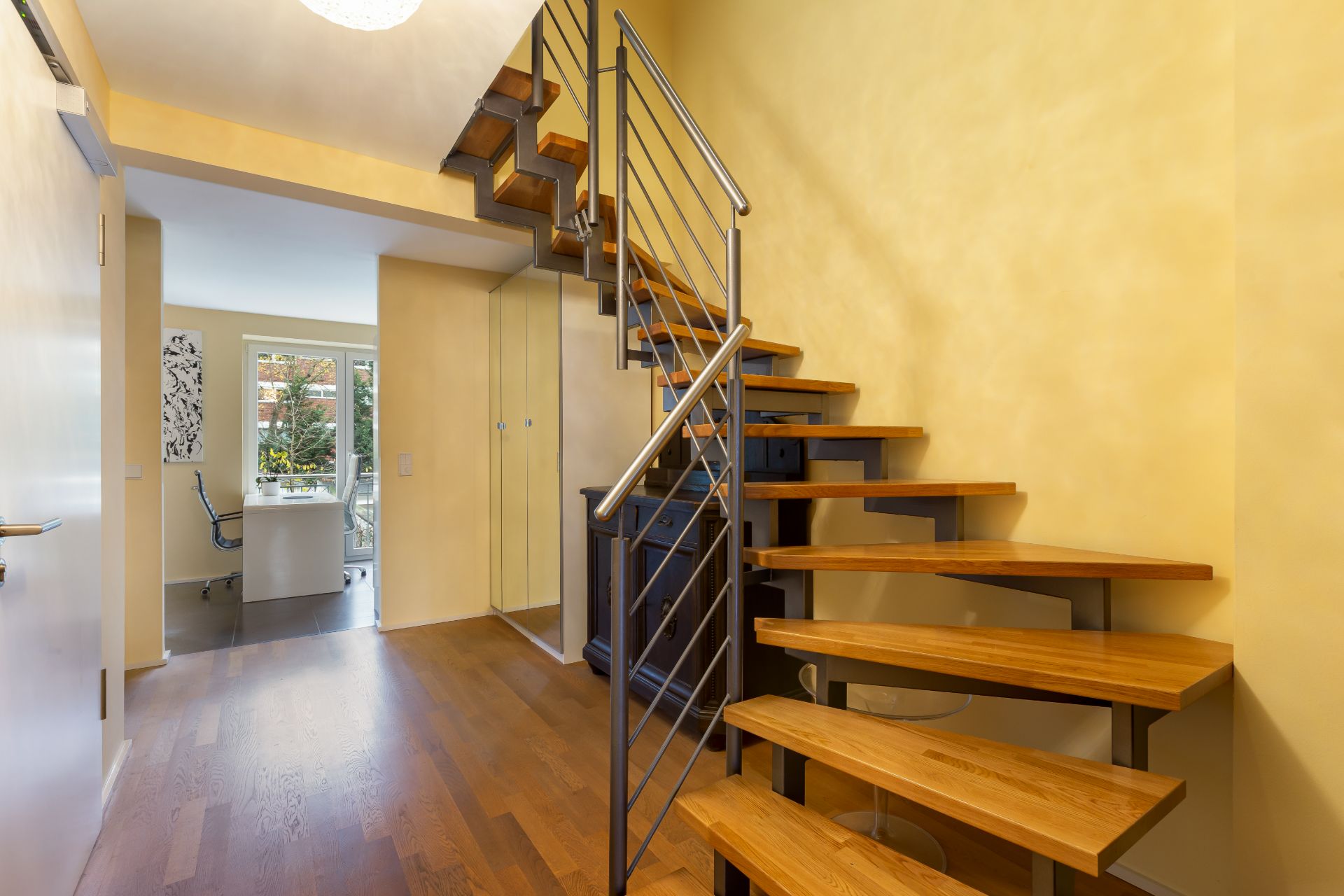 Flur mit moderner Holztreppe und Blick in ein helles Arbeitszimmer.