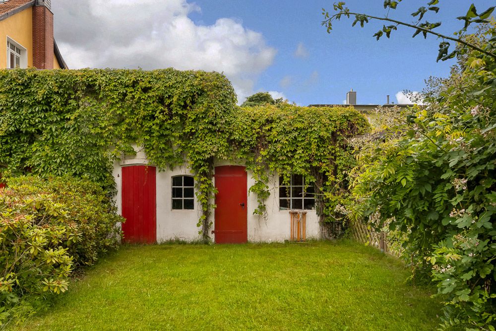 Kleine Gartenhütte mit roten Türen, überzogen von dichtem Efeu, auf einer Wiese.