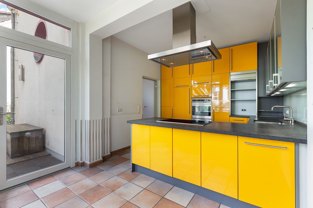 Moderne Küche mit gelben Schränken, Kochinsel und großen Fenstern.