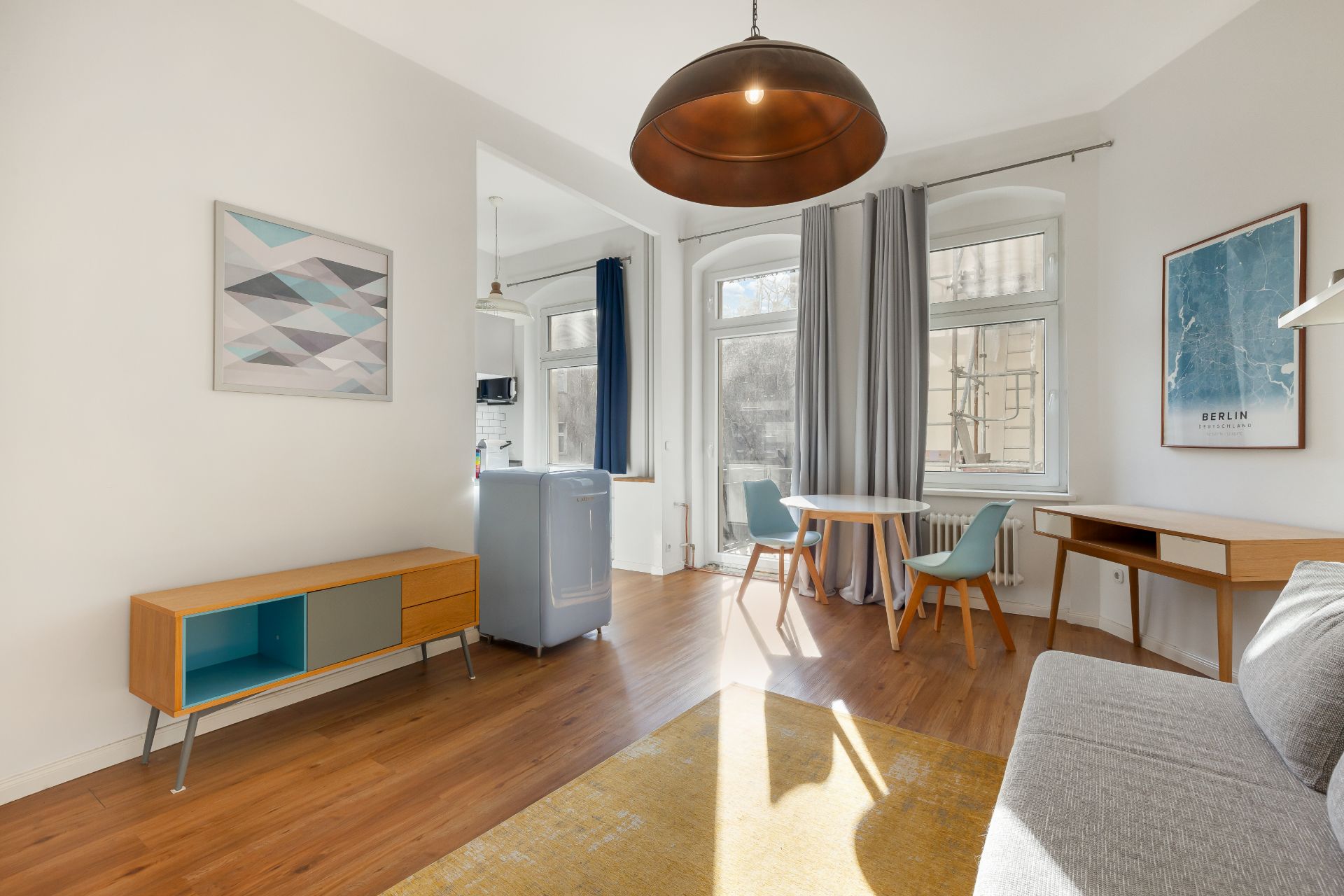 Helles Wohnzimmer mit Holzfußboden, Sofa, Esstisch, Stühlen und großem Fenster.