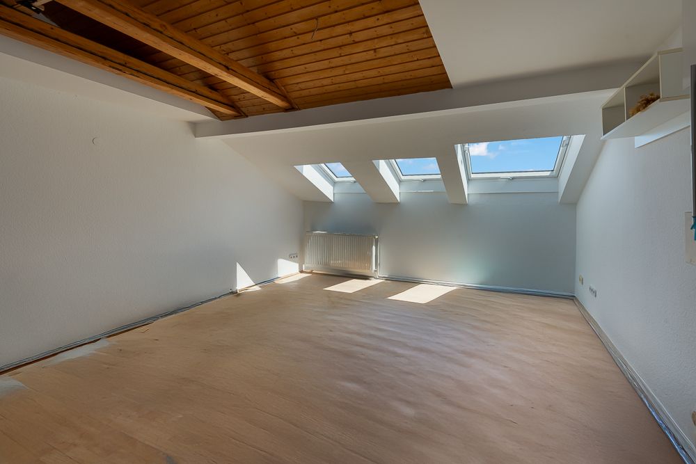 Heller Dachraum mit Holzdecke, drei Dachfenstern und hellem Laminatboden.