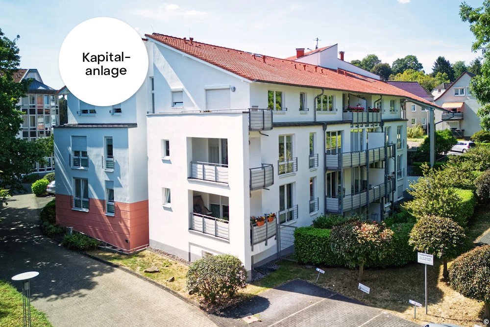 Modernes Wohnhaus mit mehreren Balkonen, Parkplatz und umliegendem Grün.