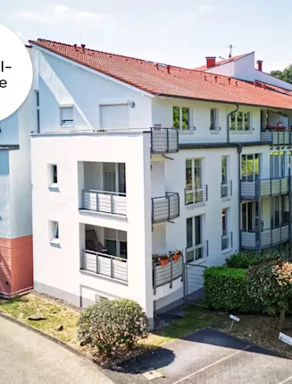 Modernes Wohnhaus mit mehreren Balkonen, Parkplatz und umliegendem Grün.