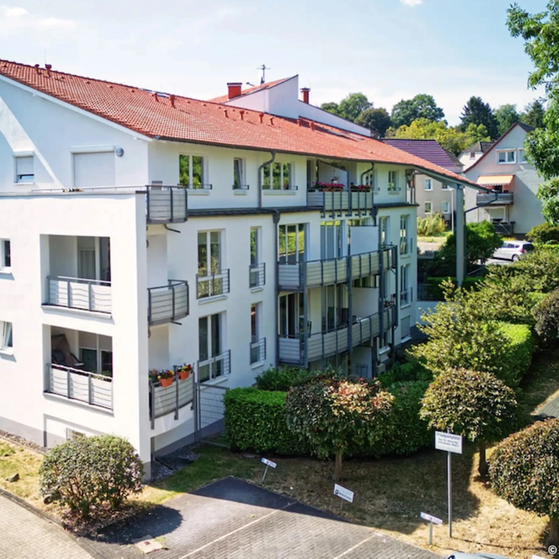 Modernes Wohnhaus mit mehreren Balkonen, Parkplatz und umliegendem Grün.