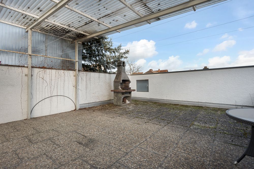 Überdachte Terrasse mit gemauertem Grill und gemustertem Steinboden.