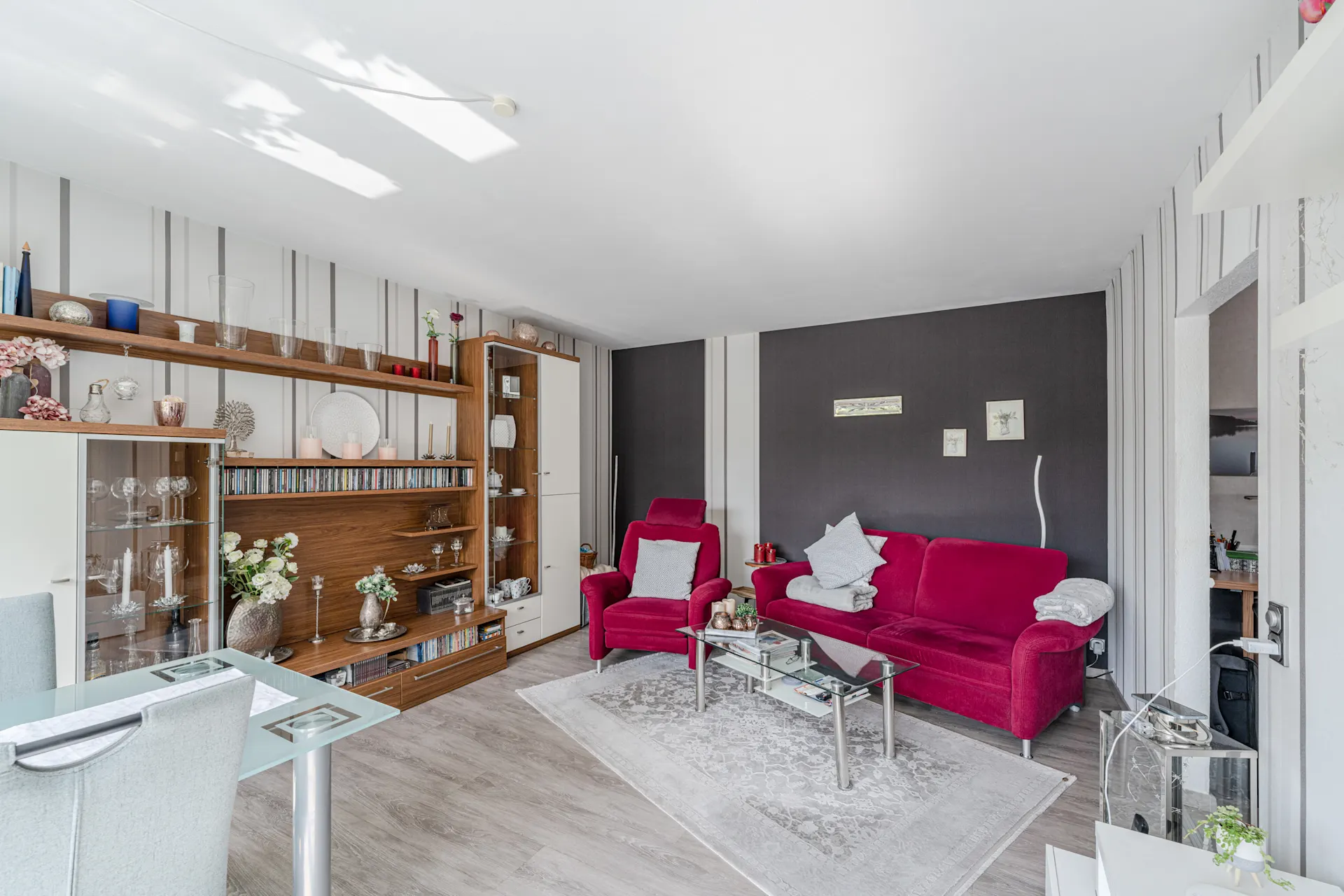 Wohnzimmer mit roten Polstermöbeln, Glastisch, Regalwand und dekorativen Elementen.