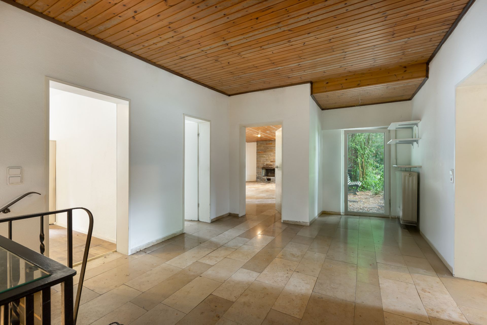 Heller Flur mit Fliesenboden, Holzbalkendecke und Zugang zu weiteren Räumen und einer Glastür zum Garten.