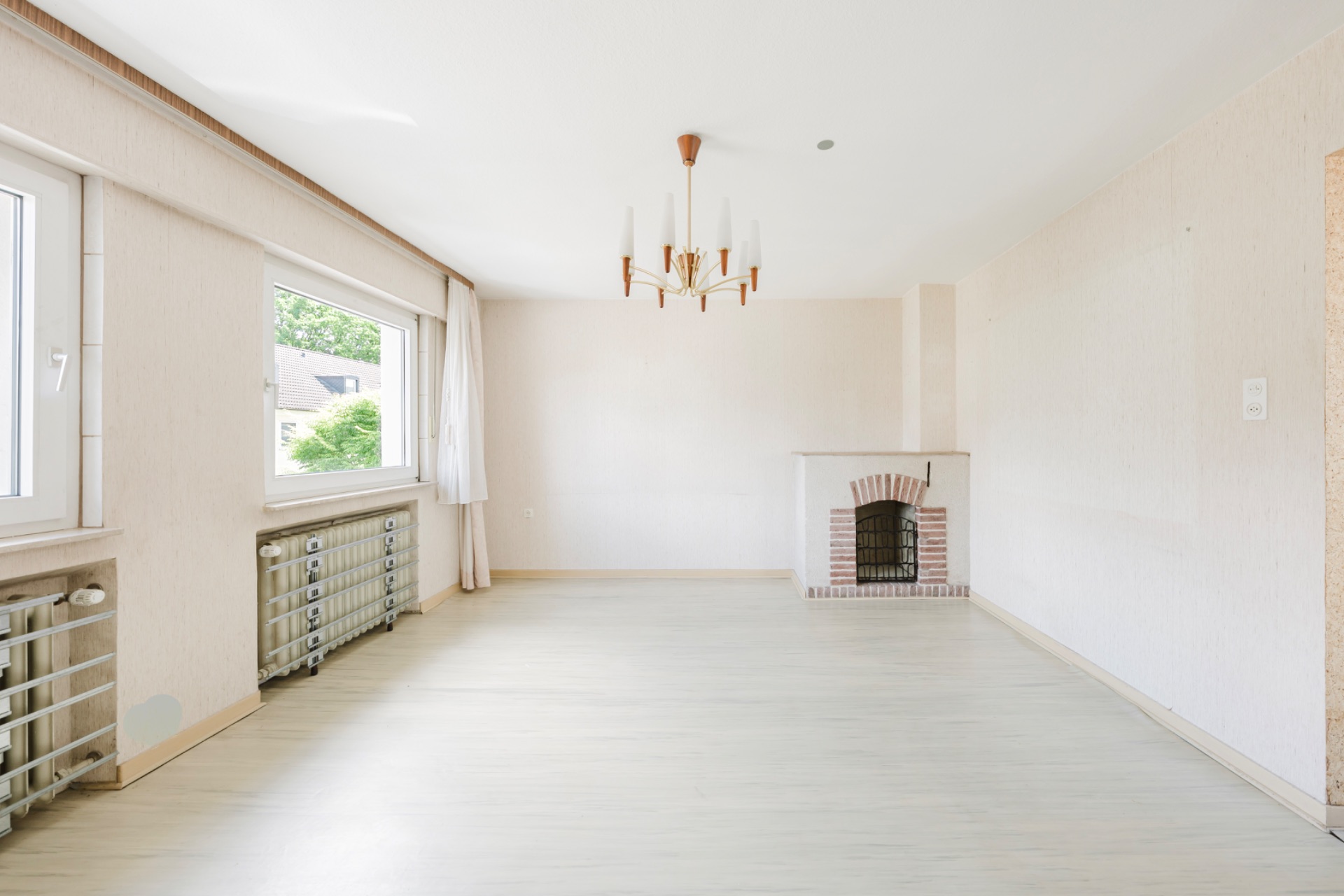 Helles Wohnzimmer mit großem Fenster, Kronleuchter und Kamin.