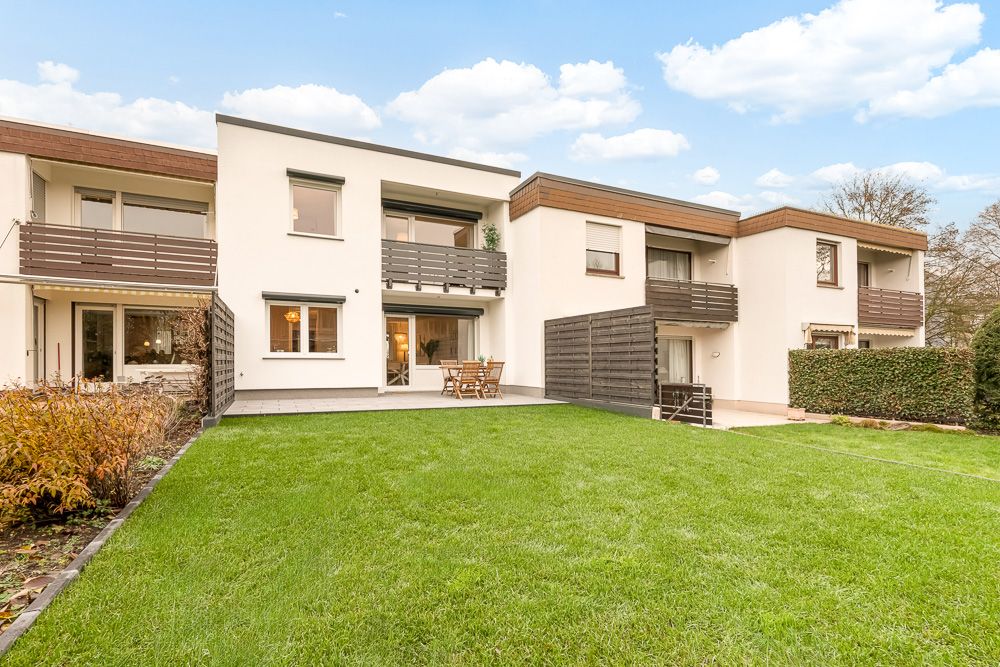 Moderne Wohnanlage mit Balkonen und Terrasse, davor grüner Rasen und Büsche.