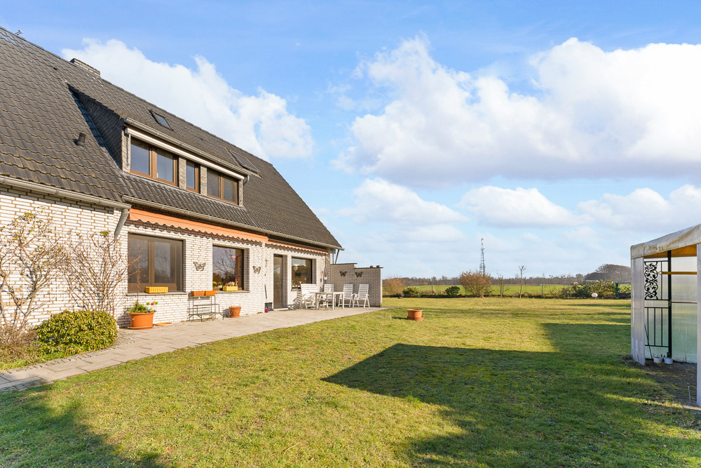 Großes Einfamilienhaus mit Terrasse und weitem Garten an einem sonnigen Tag.